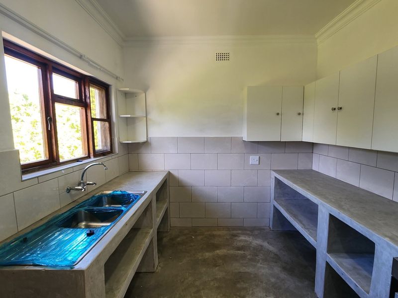 A functional kitchen space featuring concrete countertops, a double basin sink, tiled backsplash, and built-in cabinetry, currently in an unfinished state.