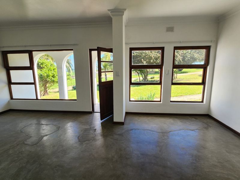An empty living room featuring polished concrete floors, timber-framed windows, and an arched doorway leading to the garden.