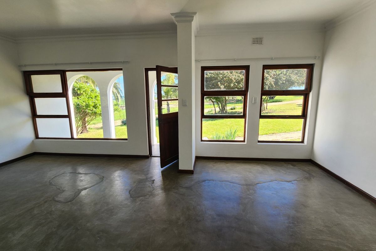 An empty living room featuring polished concrete floors, timber-framed windows, and an arched doorway leading to the garden.