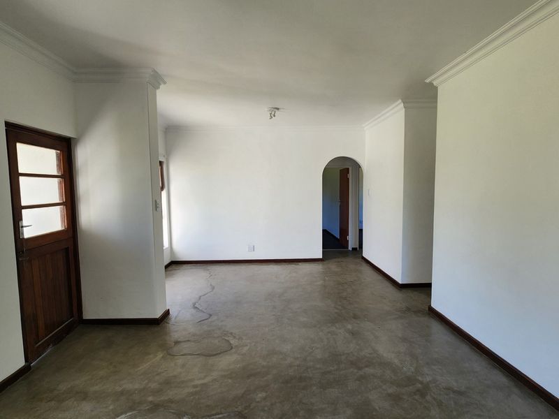 An empty living area featuring concrete flooring, an arched doorway, and crown molding, offering a blank canvas for renovation.