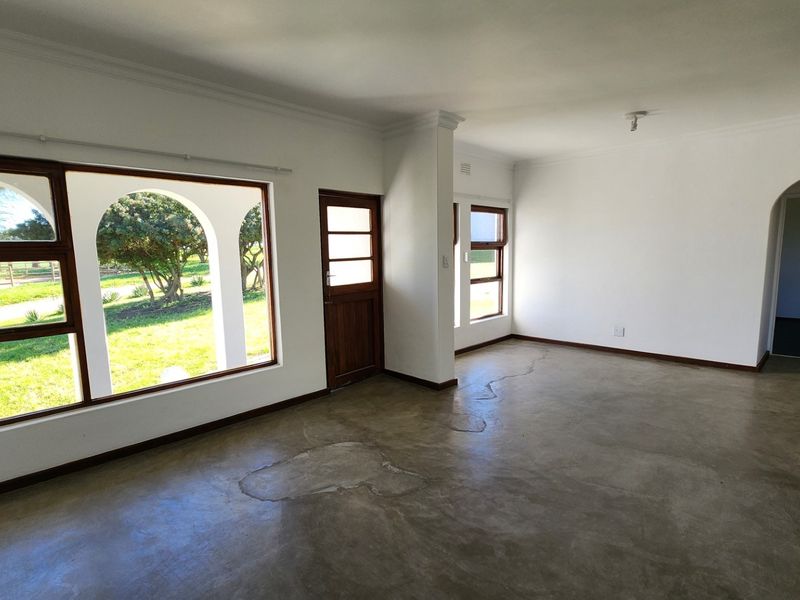 An empty living room featuring polished concrete floors, timber-framed windows with garden views, and an arched doorway leading to an adjacent space.