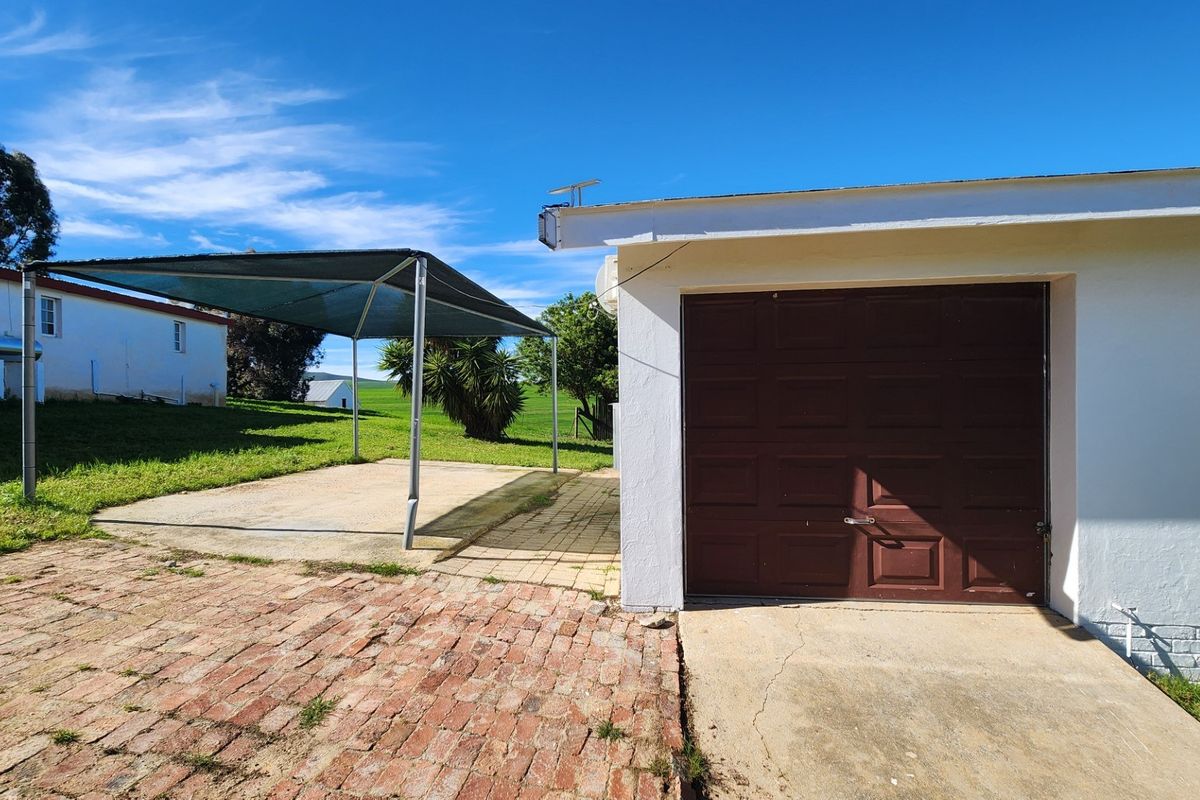 Rear exterior view featuring a single garage with a brown door, adjacent brick paving, and a shade sail structure over a concrete area.