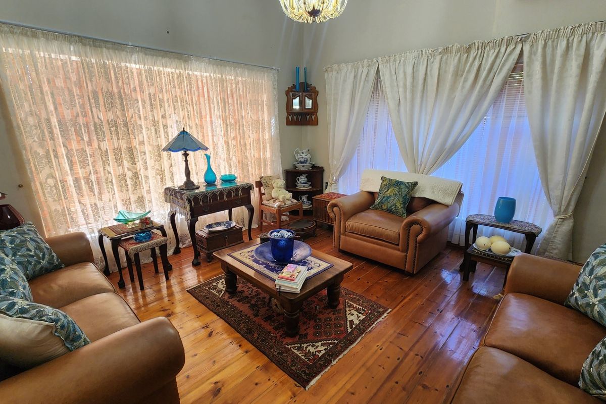 A cozy living room featuring warm hardwood flooring, a vaulted ceiling, and large windows with natural light.
