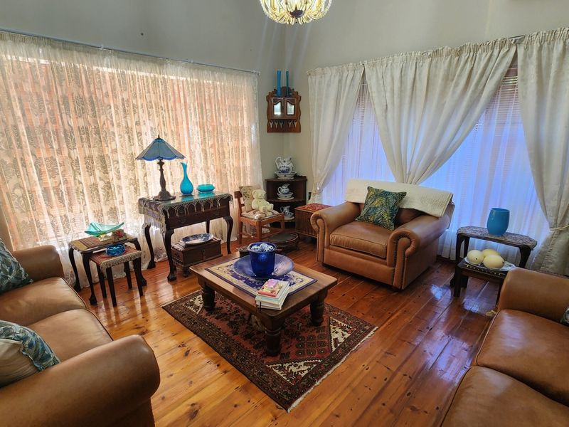 A cozy living room featuring warm hardwood flooring, a vaulted ceiling, and large windows with natural light.