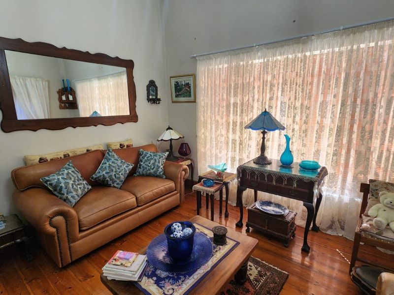 A cozy living room featuring warm hardwood flooring and a large window with sheer curtains, providing natural light to the space.