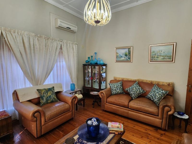 A cozy living room featuring polished timber flooring, coved cornicing, an ornate ceiling rose, and a wall-mounted split-system air conditioning unit.