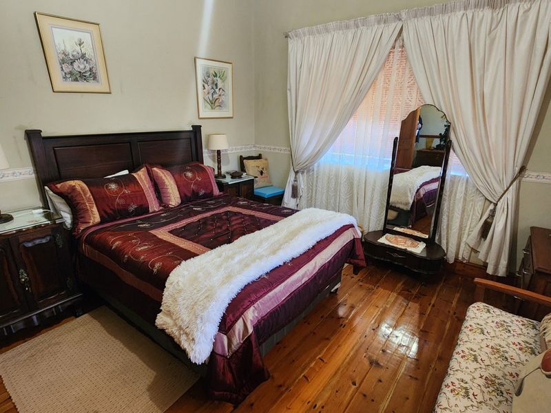 A cozy bedroom featuring polished hardwood flooring and classic window treatments, offering a warm and traditional living space.