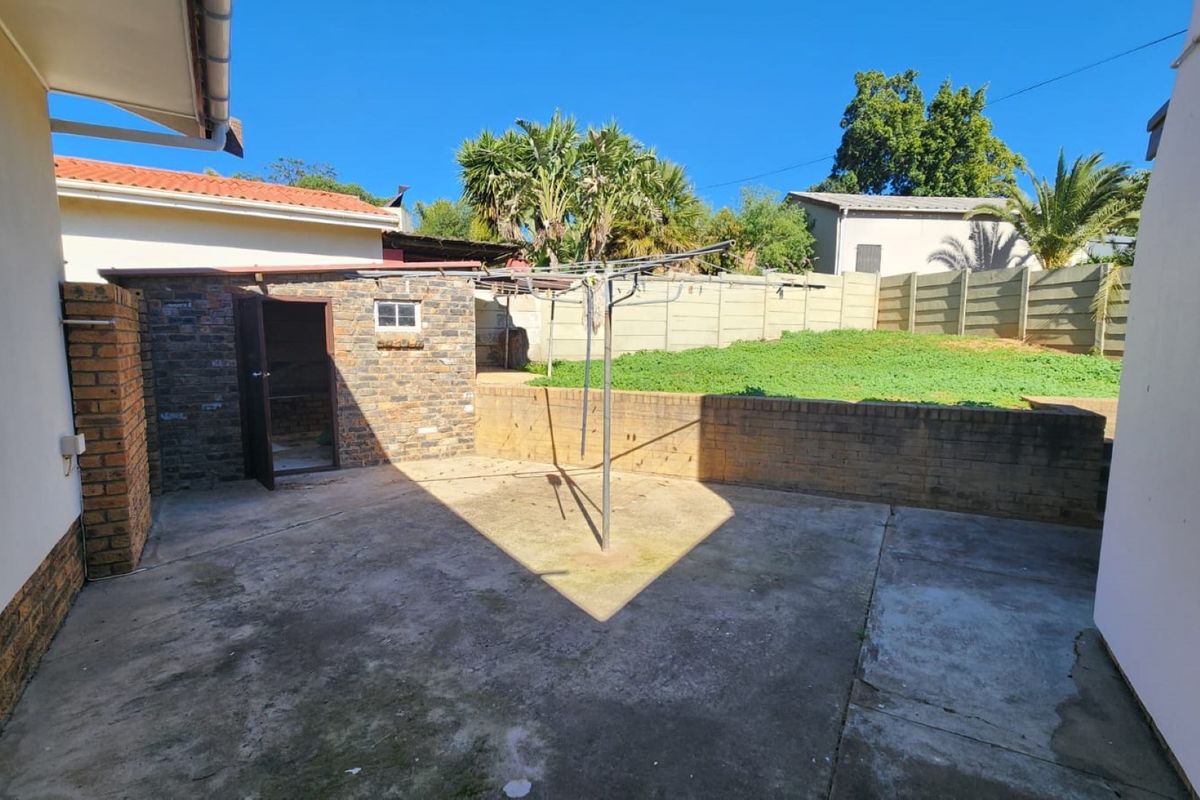 Rear exterior area featuring a concrete patio, brick outbuilding, and a raised garden section enclosed by a precast boundary wall.