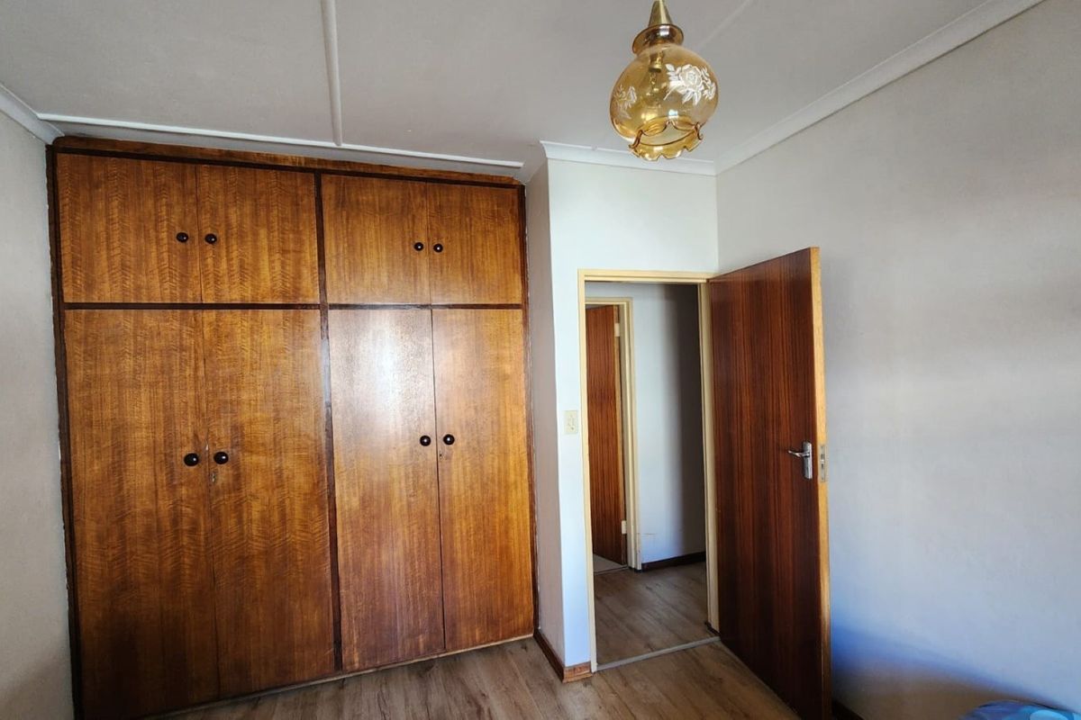 A bedroom featuring built-in wooden cupboards, laminate flooring, and a classic ceiling light fixture, offering a clean and functional space.