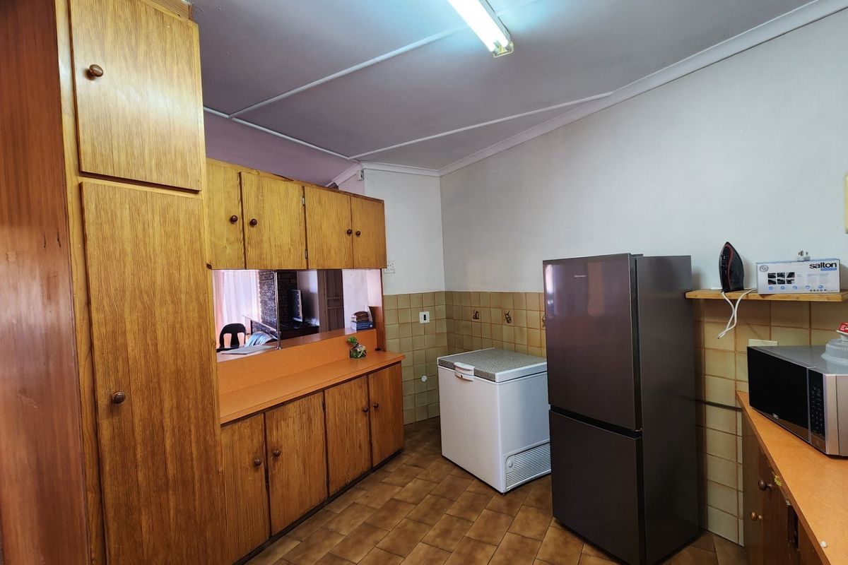 A functional kitchen featuring traditional wooden cabinetry, tiled splashbacks, and a convenient pass-through window connecting to the adjacent living area.