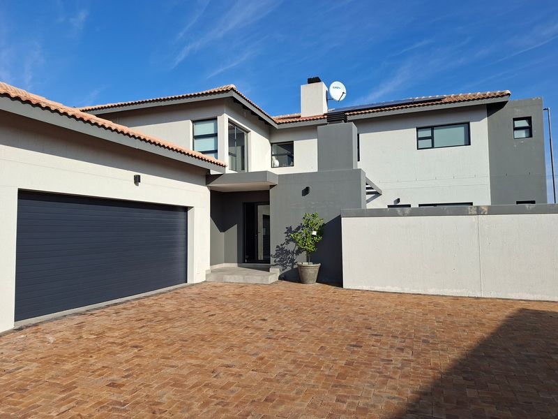 Modern double-story residential home featuring a paved driveway, integrated double garage, and contemporary architectural finishes under a tiled roof.