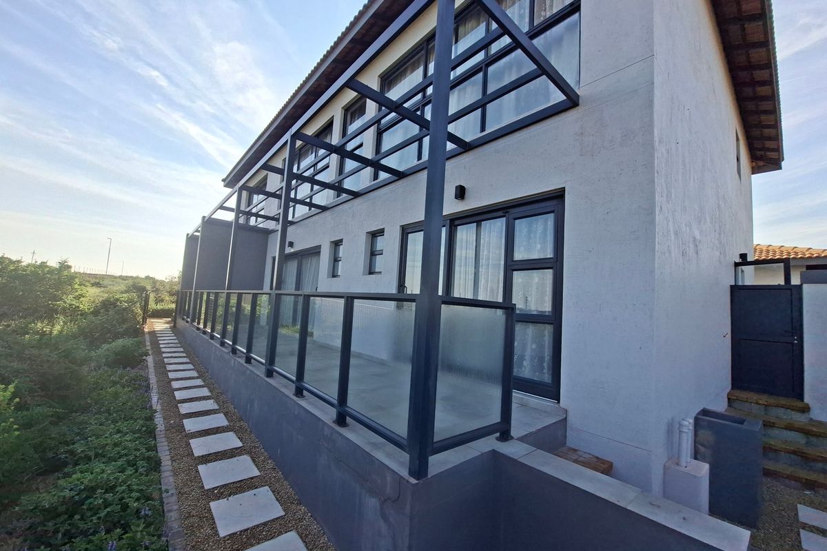 Rear elevation of a modern two-story house featuring a spacious concrete patio, steel pergola structure, and glass balustrades overlooking a landscaped garden path.