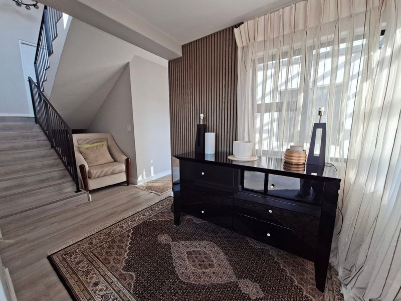 A well-maintained hallway featuring a modern staircase with a metal balustrade, timber-look flooring, and a stylish slatted timber feature wall.