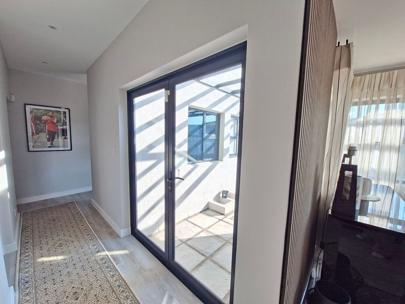 A modern hallway featuring laminate flooring, recessed lighting, and a stylish timber slat wall accent, leading through glass doors to an outdoor patio area.