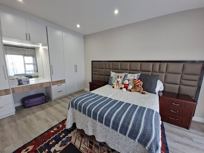 A well-maintained bedroom featuring modern built-in cupboards with an integrated vanity, recessed ceiling lighting, and a large upholstered headboard.