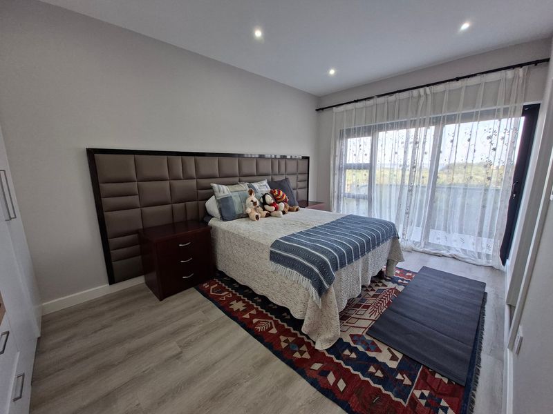 A well-maintained bedroom featuring modern laminate flooring, recessed downlighting, and a large sliding glass door providing access to a balcony.