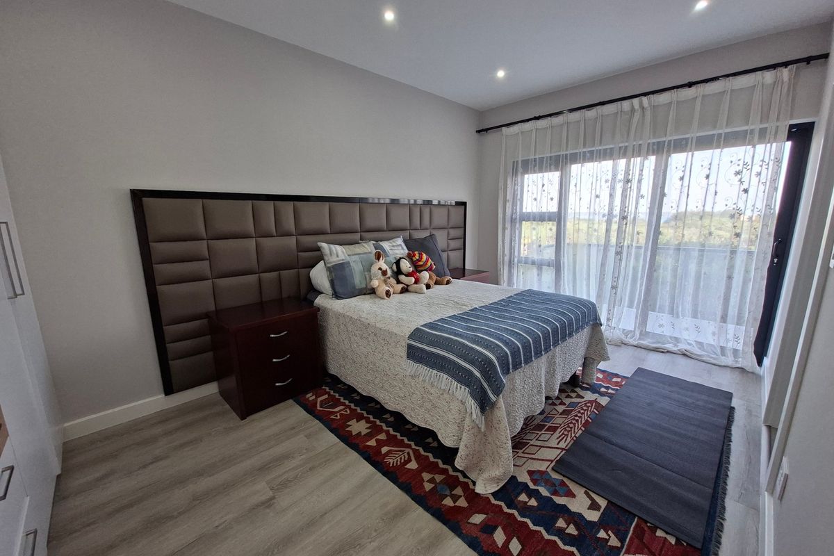 A well-maintained bedroom featuring modern laminate flooring, recessed downlighting, and a large sliding glass door providing access to a balcony.