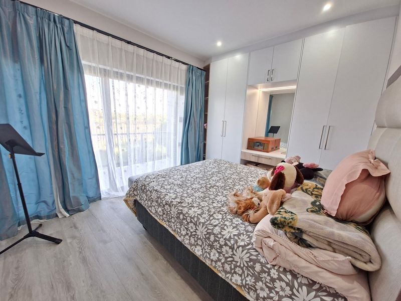 A well-maintained bedroom featuring modern built-in cupboards, laminate flooring, and a sliding glass door providing natural light.