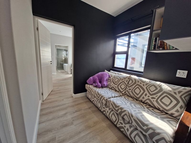A modern bedroom featuring dark accent walls, light laminate flooring, and built-in shelving, with an adjoining view into a contemporary bathroom.