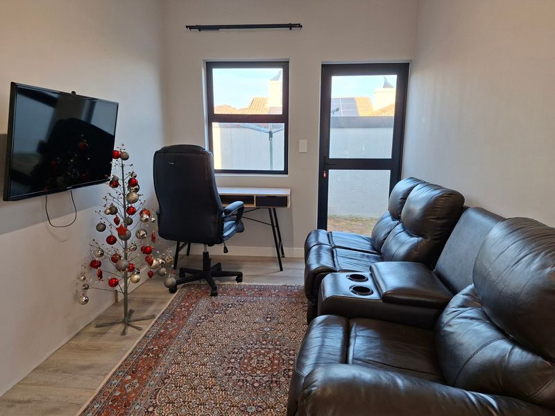 A compact living area featuring laminate flooring, modern aluminium window and door frames, and direct access to an outdoor space.