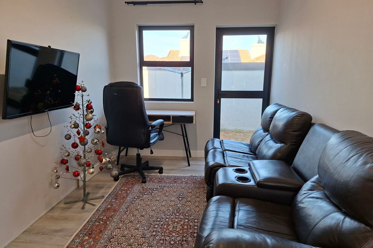 A compact living area featuring laminate flooring, modern aluminium window and door frames, and direct access to an outdoor space.