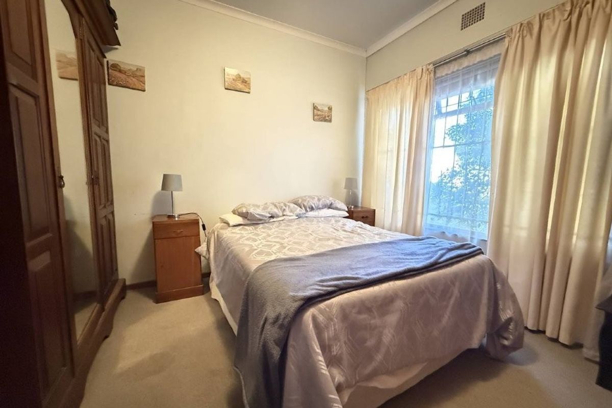 A standard bedroom featuring neutral walls, carpeted flooring, and a window with curtains, providing a functional and comfortable living space.