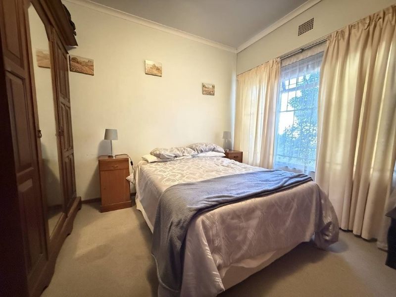 A standard bedroom featuring neutral walls, carpeted flooring, and a window with curtains, providing a functional and comfortable living space.