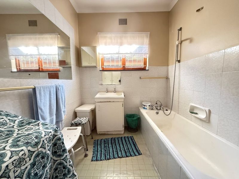 A functional bathroom featuring a bathtub with shower mixer, vanity cabinet with basin, and wall-mounted mirror, offering a dated but practical layout.