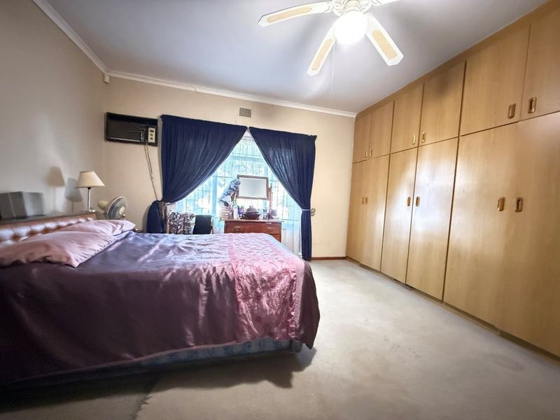 A spacious bedroom featuring extensive built-in wooden cabinetry, a ceiling fan, and a wall-mounted air conditioning unit.