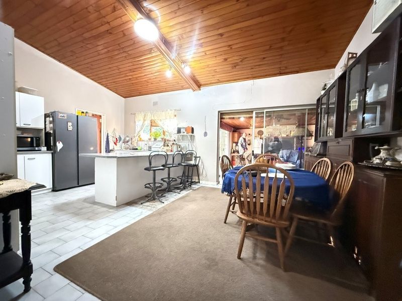 Open-plan kitchen and dining area featuring a vaulted timber ceiling, tiled flooring, and direct access to an outdoor patio through sliding glass doors.