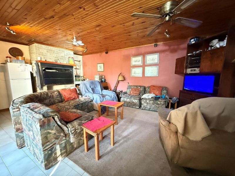 Spacious living room featuring a timber-clad ceiling, a brick fireplace, and a ceiling fan, offering a dated interior ready for modernization.