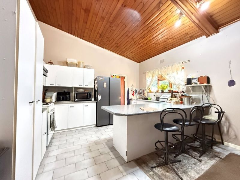 A functional kitchen featuring white cabinetry, laminate countertops, a central island, and a distinctive timber tongue and groove vaulted ceiling.