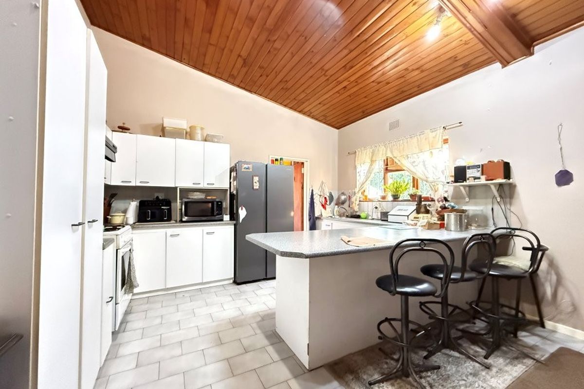 A functional kitchen featuring white cabinetry, laminate countertops, a central island, and a distinctive timber tongue and groove vaulted ceiling.