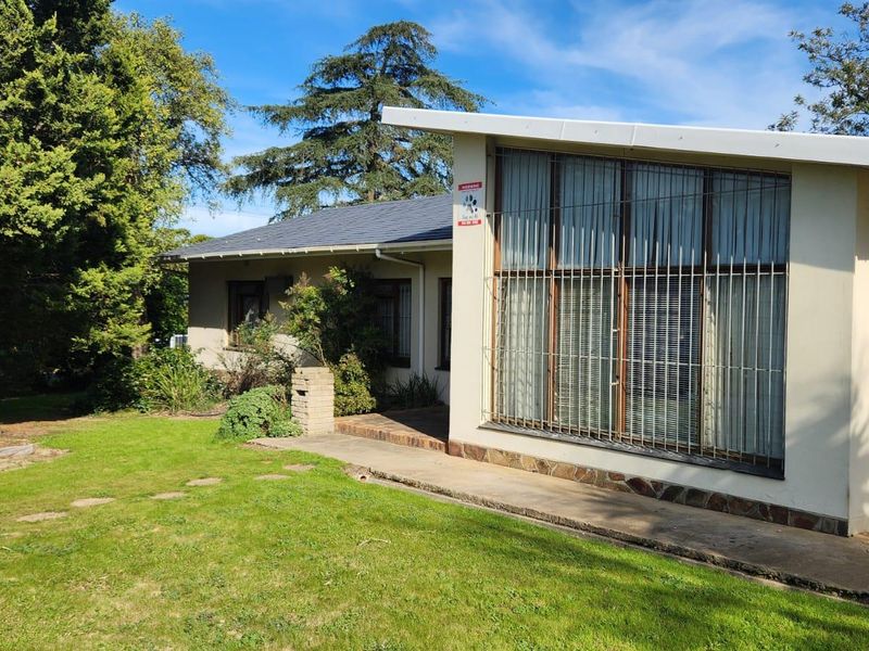 Rear view of the house featuring a concrete walkway, security bars on large windows, and stone cladding accents set against a garden.