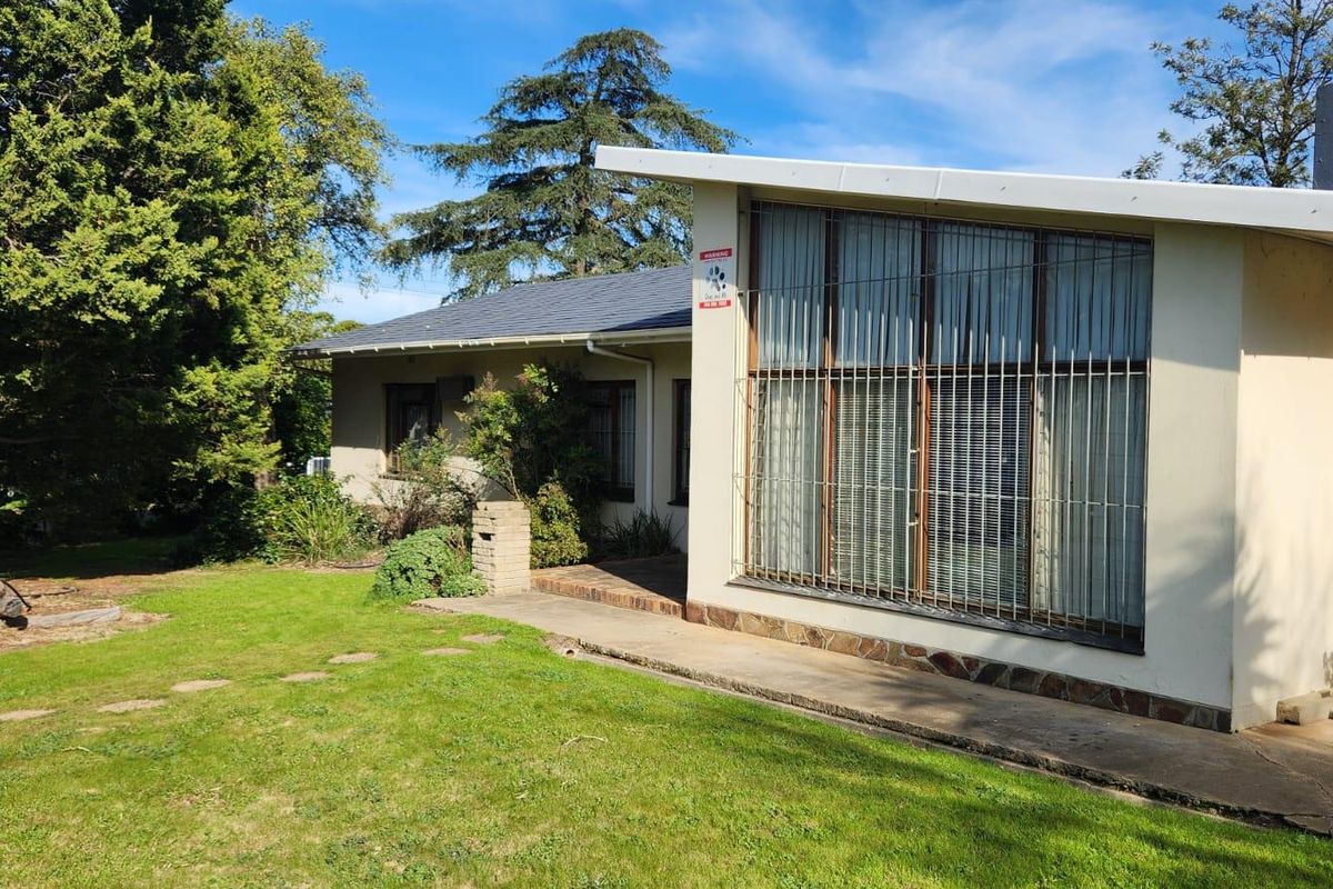 Rear view of the house featuring a concrete walkway, security bars on large windows, and stone cladding accents set against a garden.
