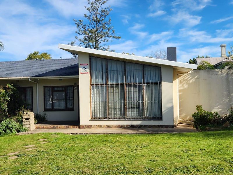 Front elevation of a house featuring a distinctive skillion roofline, large windows with security bars, and a paved patio area set within a garden.