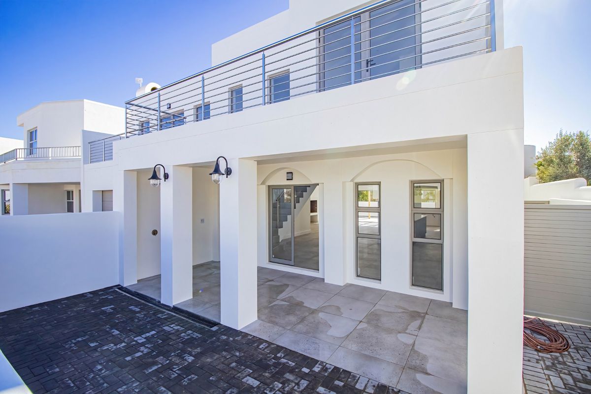 A modern rear exterior view featuring a covered patio with tiled flooring, stainless steel balustrades on the upper balcony, and clean white architectural finishes.