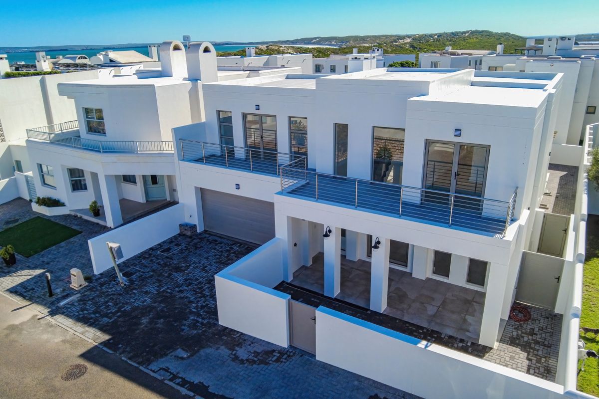 Aerial view of a modern white multi-story residential property featuring a paved driveway, double garage, and an upper-level balcony with stainless steel railings.