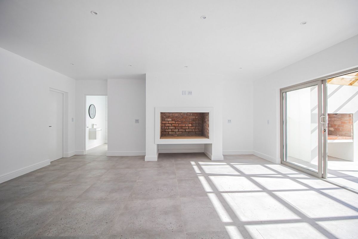 Bright and spacious living area featuring large sliding glass doors, modern tiled flooring, and a characterful built-in fireplace with exposed brick detailing.
