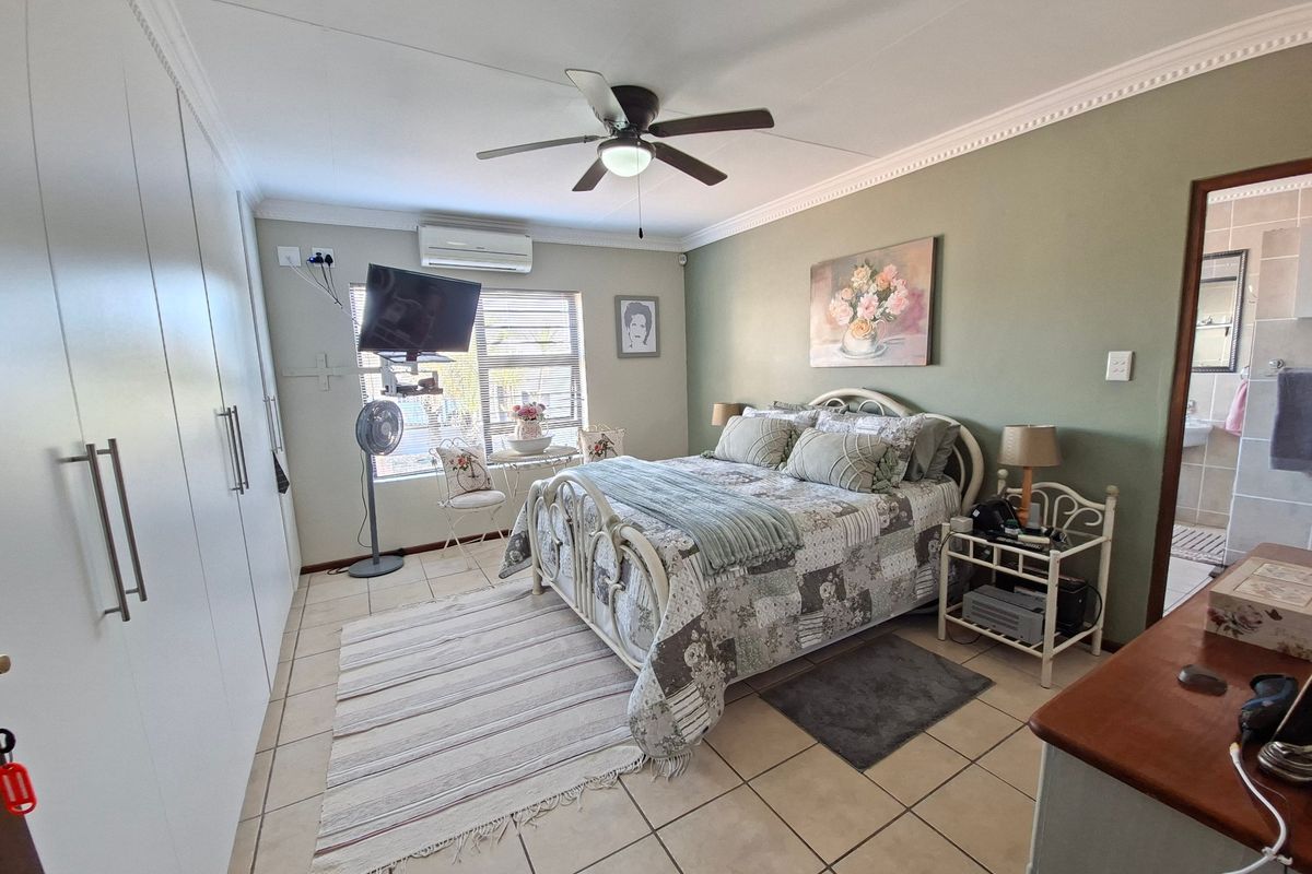 A well-maintained bedroom featuring built-in cupboards, tiled flooring, a ceiling fan, and a split-system air conditioner for climate control.