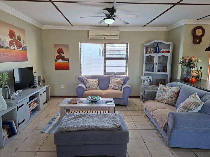 A comfortable living room featuring tiled flooring, a ceiling fan, and a wall-mounted air conditioning unit.