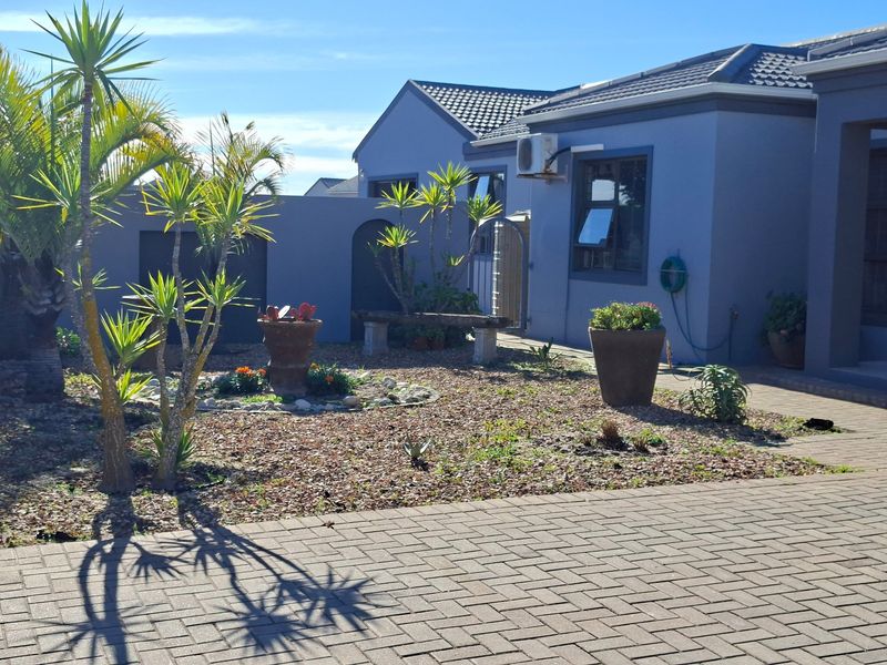 A well-maintained rear exterior view featuring a paved courtyard, landscaped garden area, and modern grey-toned building facade with tiled roofing.