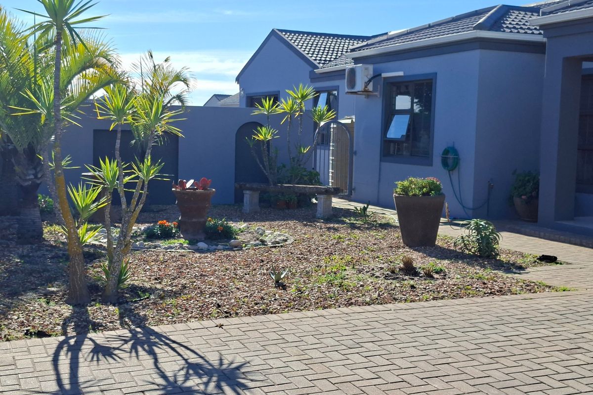 A well-maintained rear exterior view featuring a paved courtyard, landscaped garden area, and modern grey-toned building facade with tiled roofing.