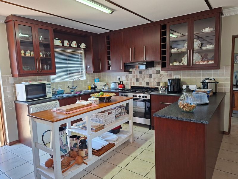 A functional kitchen featuring dark wood cabinetry, glass-fronted display units, a stainless steel gas stove, and tiled backsplash with neutral ceramic flooring.