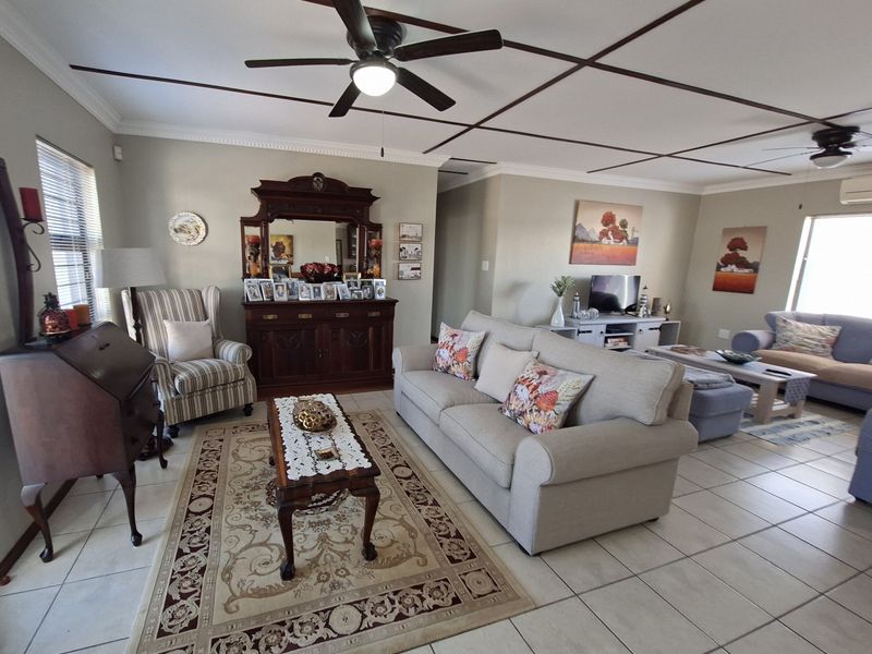 Spacious living room featuring tiled flooring, crown molding, and a distinctive grid-pattern ceiling design with integrated ceiling fans.