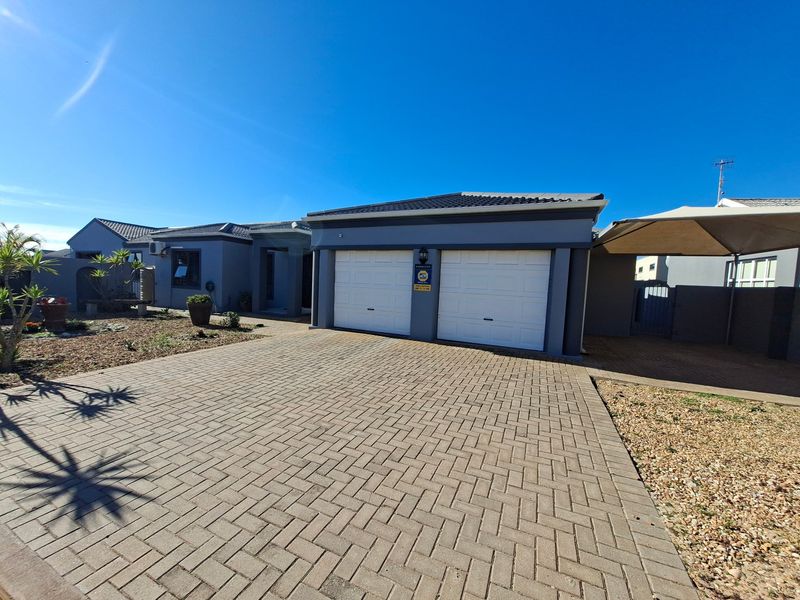 Front elevation of a modern house featuring a double garage, paved driveway, and an additional shade sail carport area.