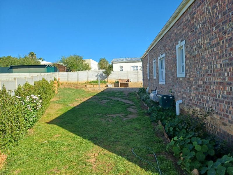 Rear garden area featuring a brick facade, precast boundary wall, and a built-in outdoor braai area with lawn space.