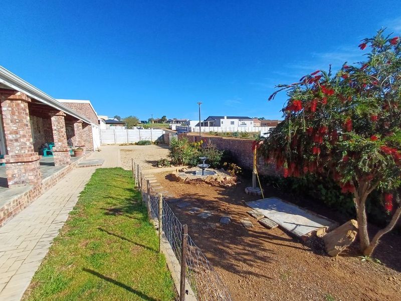 Rear exterior view of the property featuring a covered brick patio, paved walkway, and a landscaped garden area with boundary walling.