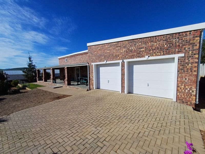 Front view of a brick house featuring a double garage, paved driveway, and a covered patio area.