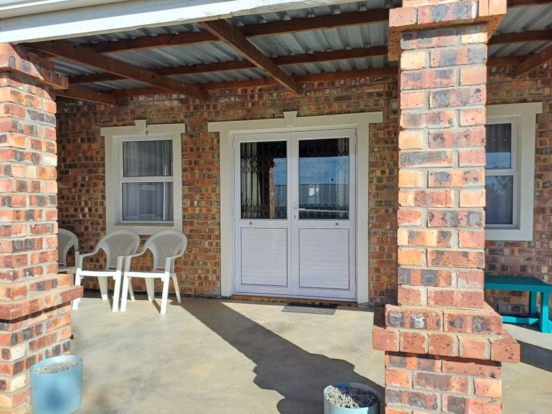 A covered patio area featuring exposed brickwork, timber roof beams, and double glass doors with security gates.